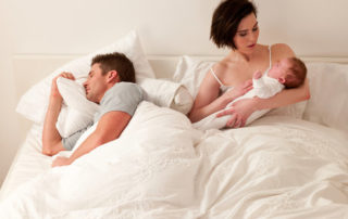 Young mum in bed with crying baby while dad sleeps