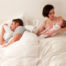 Young mum in bed with crying baby while dad sleeps
