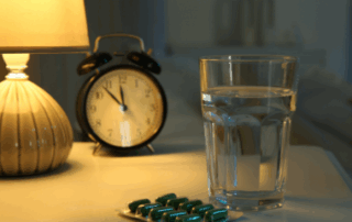 Melatonin pill by clock and water glass on table near bed