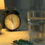 Melatonin pill by clock and water glass on table near bed