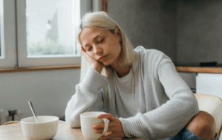 Tired woman holding coffee at table